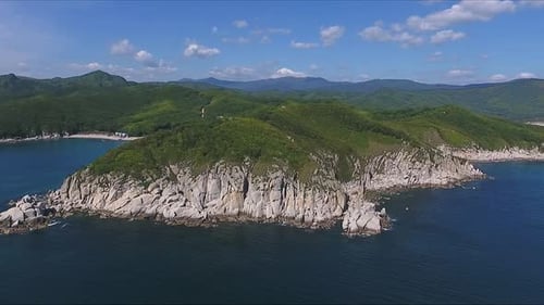 Aerial Shot Moving Along the Coastline of Deep Blue Sea Along a Dramatic Cliff Edge on Sunny Day