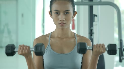 Young Woman Doing Dumbbell Curls at Gym