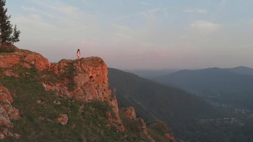 A Young Woman Approaches the Edge of the Rock and Raises Her Hands Happily