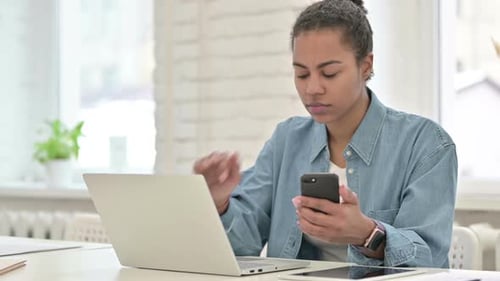 Woman Uses Phone While Working on Laptop