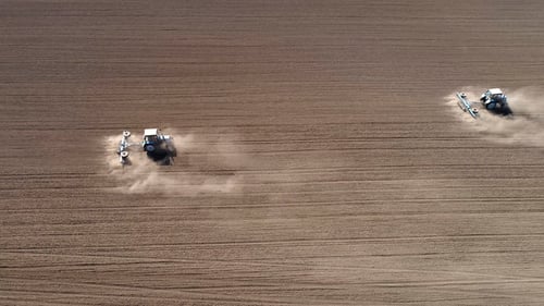 Aerial View of Agricultural Tractors Cultivating Field.