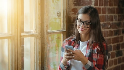 Smiling Woman Using Phone Near Sunny Window