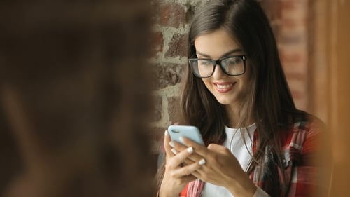 Smiling Woman Using Smartphone Near Brick Wall