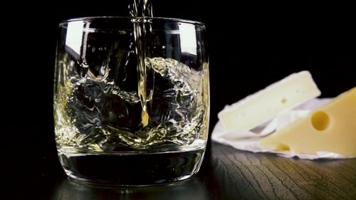 White Wine Pours into Glass Beside Gourmet Cheese