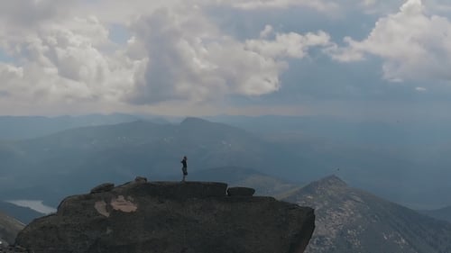 Aerial Shot of Silhouette of a Male Climber Standing on Top of a Mountain Happily Raising His Hands.
