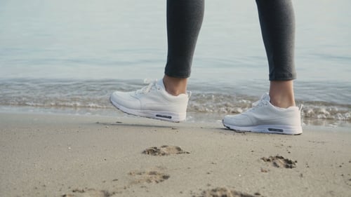 Female Legs in White Sneakers Walks at the Sea
