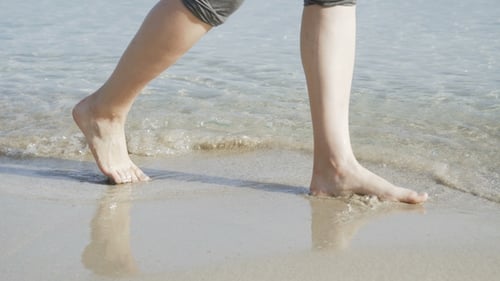 Female Legs Barefoot Walks at the Sea on the Splashing Waves.