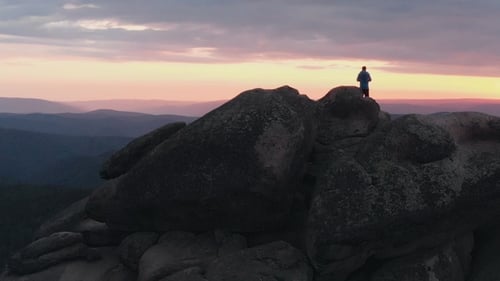 Tiro de Drone de homem solitário em pé no topo de uma montanha e apreciando o pôr do sol