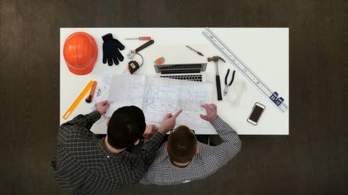Architekt arbeitet am Laptop, während sein Kollege mehr Zeichnungen mitbringt