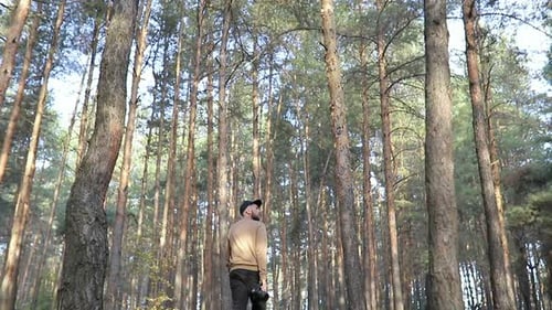 Blick von unten auf einen Mann, der mit Kamera durch den Wald geht