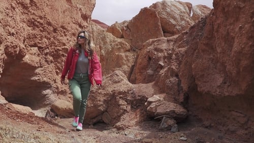 Touristin in Sonnenbrillen geht auf ein ungewöhnliches Terrain. Rote Berge und rote Erde wie auf dem Mars.