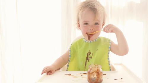 Adorable Child Eating Food with Spoon in High Chair