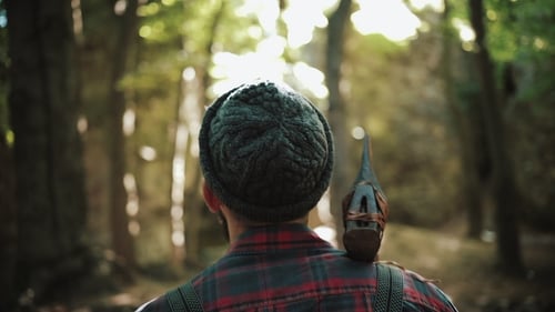Walking Bearded Lumberjack with Axe Man in a Cap Walks Through the Woods in Search of the Tree