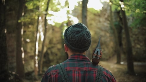 Walking Bearded Lumberjack with Axe Man in a Cap Walks Through the Woods in Search of the Tree