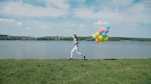 Happy Young Girl Runs with Colourful Balls on the Summer Bay