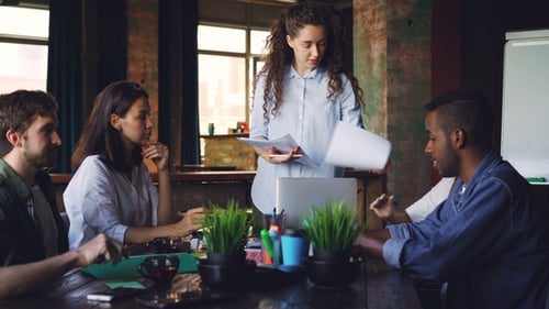 Confident Young Woman Director Is Giving Documents To Her Employees and Talking To Group of People