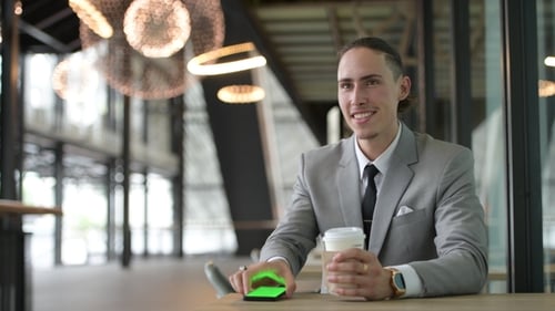 Man in Suit Using Phone with Coffee Indoors