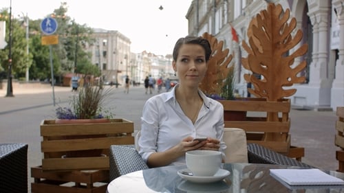 Young Woman Drinking Coffee and Using Her Mobile Phone in a Outdoor Cafe