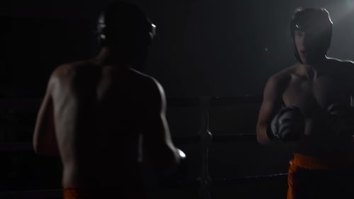Zwei Jungs in Helmen und Boxhandschuhen schlagen im Ring im Dunkeln