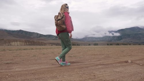 Hiker Walks the Mountainous Terrain in Inclement Weather. Clouds Below the Mountain Peaks. Girl with