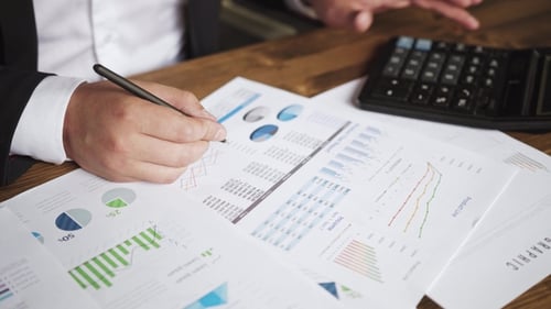 of a Businessman Hands with Pen Working at Office Desk and Analyzing Graphs and Charts and Writing