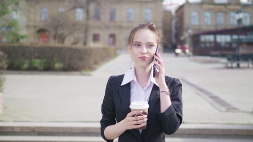 Businesswoman in City Using Smart Phone with Takeaway Coffee