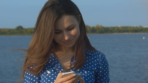 Smiling Woman Using Smartphone by the Water