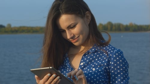 Woman Using Tablet Device Near a Body of Water