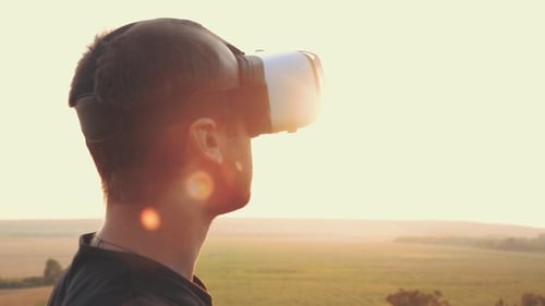 Young Man Uses Virtual Reality Glasses in Nature in a Beautiful Sunset