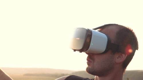 Young Man Uses Virtual Reality Glasses in Nature in a Beautiful Sunset