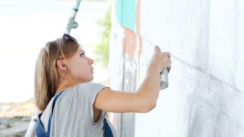 Beautiful Girl Making Graffiti of Big Female Face with Aerosol Spray on Urban Street Wall