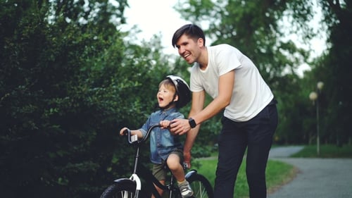 of Happy Young Man Loving Father Teaching His Child To Cycle in Green Park in Summer, Little Boy Is