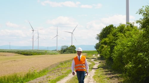 Engineer Walks Past Wind Turbines on Sunny Day
