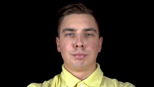 The Young Man Actively Moves His Lips. A Man Stands on a Black Background. A Man Blows Air and His