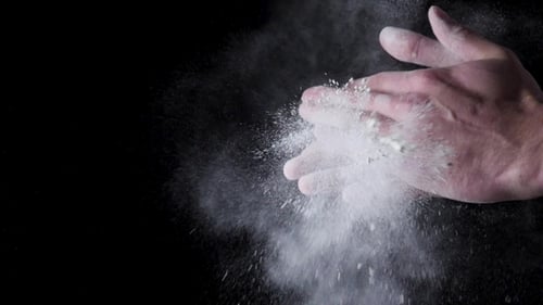 Die
Hände des Küchenchefs klatschen mit Mehl auf schwarzem Hintergrund. Rahmen. Chefkoch klatscht mit Mehl in die Hände