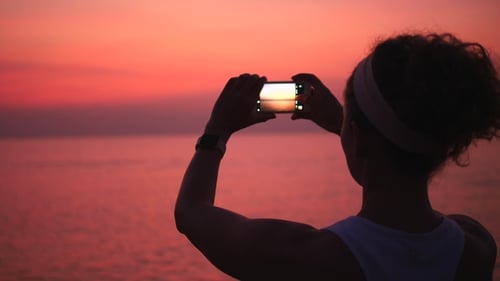 Woman Silhouette Taking Pictures Of Sea At Sunset With Smartphone