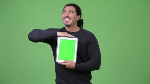 Heureux bel homme pensant tout en montrant une tablette numérique