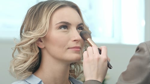 Applying Blush Makeup with Brush To Cheekbones of Smiling Young Woman