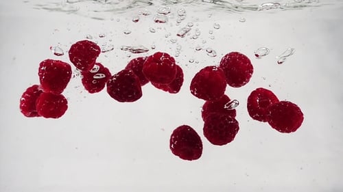 A Beautiful Raspberry Falls Into the Water with Bubbles in