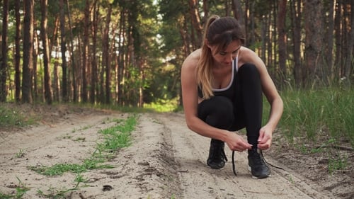 Woman Tying Shoelaces Before Running in Forest