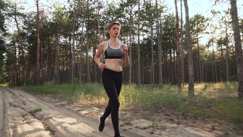 Young Woman Running Through Woods in Sports Shoes at Sunset