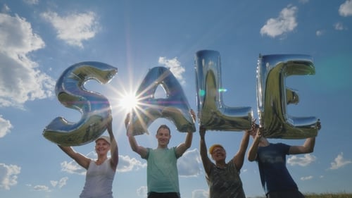 Four People Hold Silver 'SALE' Balloons in Sunlight