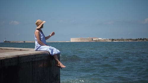 Young Woman in a Blue Dress Sits on a Wooden Pier on the Lake
