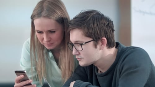 Two Young Friends Sitting at Table in School and Working on Smartphone