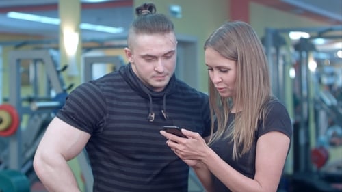 Young Woman at the Gym Adding Number of Her Fitness Instructor To Phone Contact List