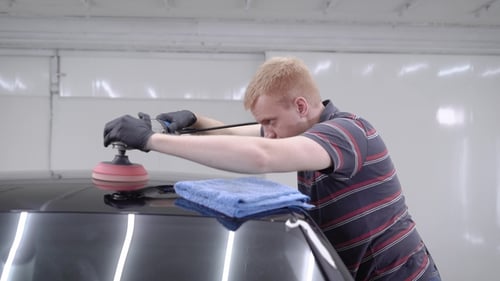 Man Polishing Black Car in Bright Garage