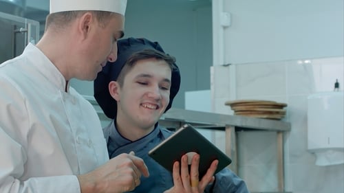 Chief Chef Showing Cook Trainee in Hat Something Funny on Digital Tablet