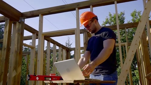 Builder Is Looking on a Screen of Laptop on a Construction Site of House, Taking Building Level and