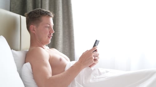 Man Uses Smartphone Lying in Bed at Home