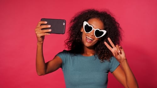 Smiling Happy African American Woman with Curly Hair in Green T-shirt Making Selfie on Smartphone